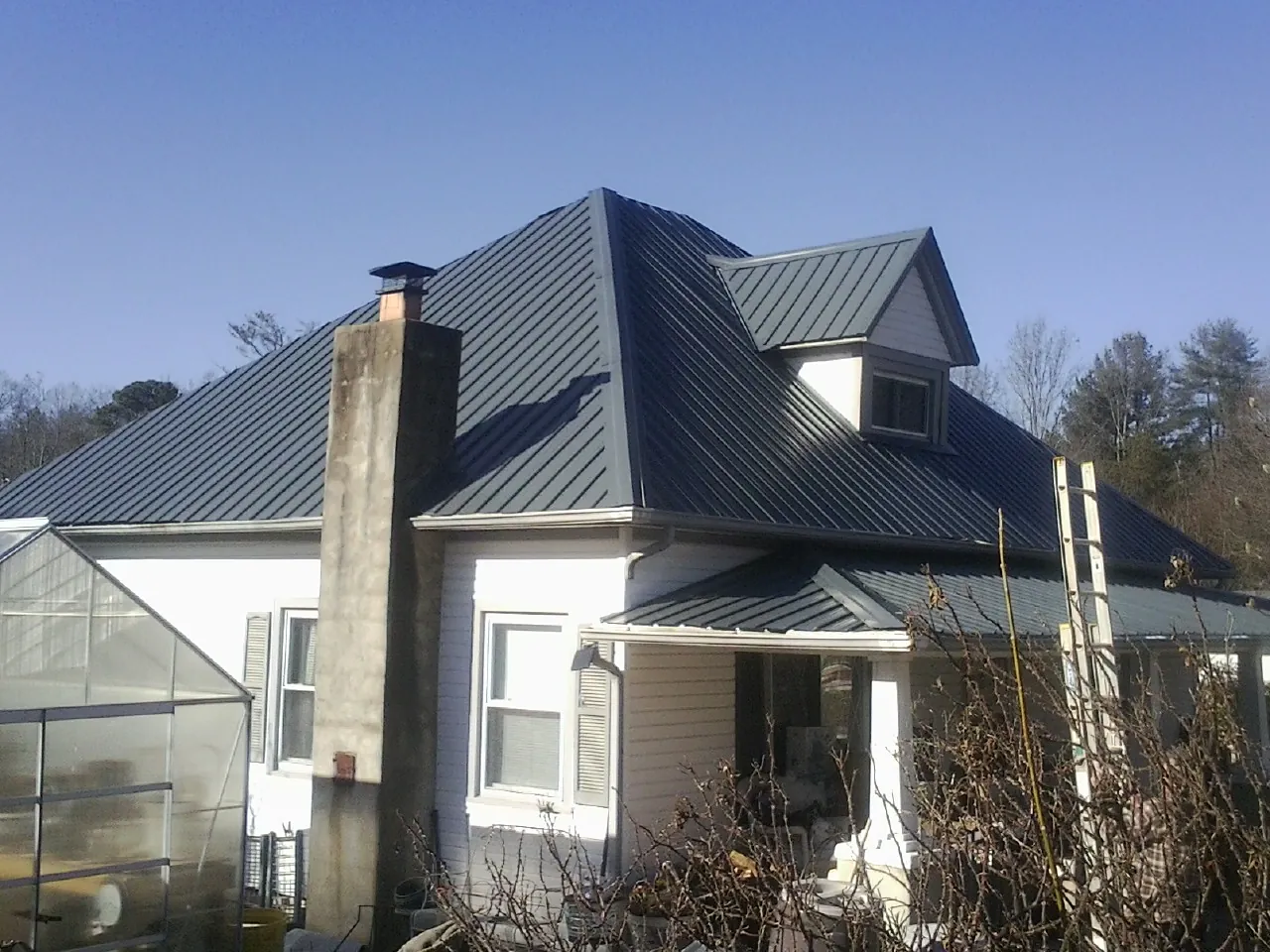 Dark blue standing seam metal roof on a white farmhouse with dormer — Slate & Tile Roof Repair by Roofing Brothers in Dobbs Ferry