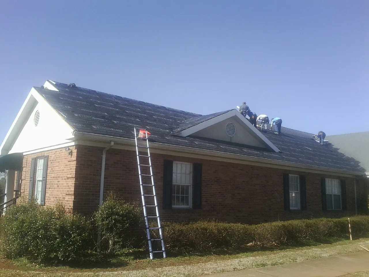 Crew tearing shingles off a brick ranch roof with a ladder set — Metal Roof Repair work by our crew in Dobbs Ferry