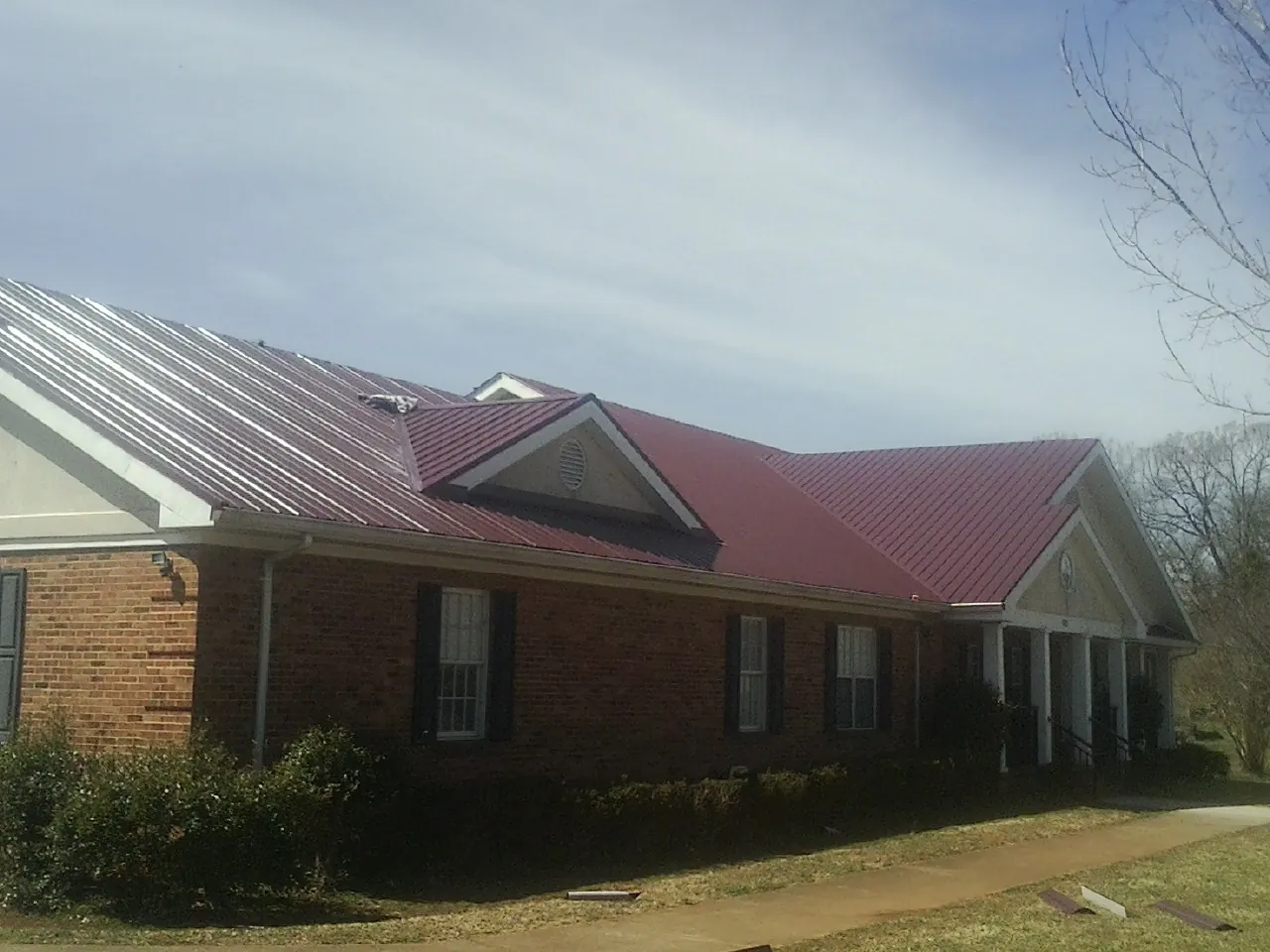 Red metal roof with gabled entries on a long brick building, from a Hail Damage Roof Repair job in Dobbs Ferry