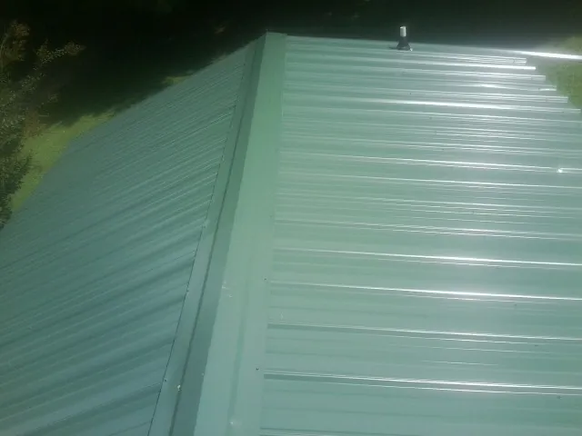 New green metal panels meeting at the ridge of a roof — Flat Roof Repair work by our crew in Dobbs Ferry