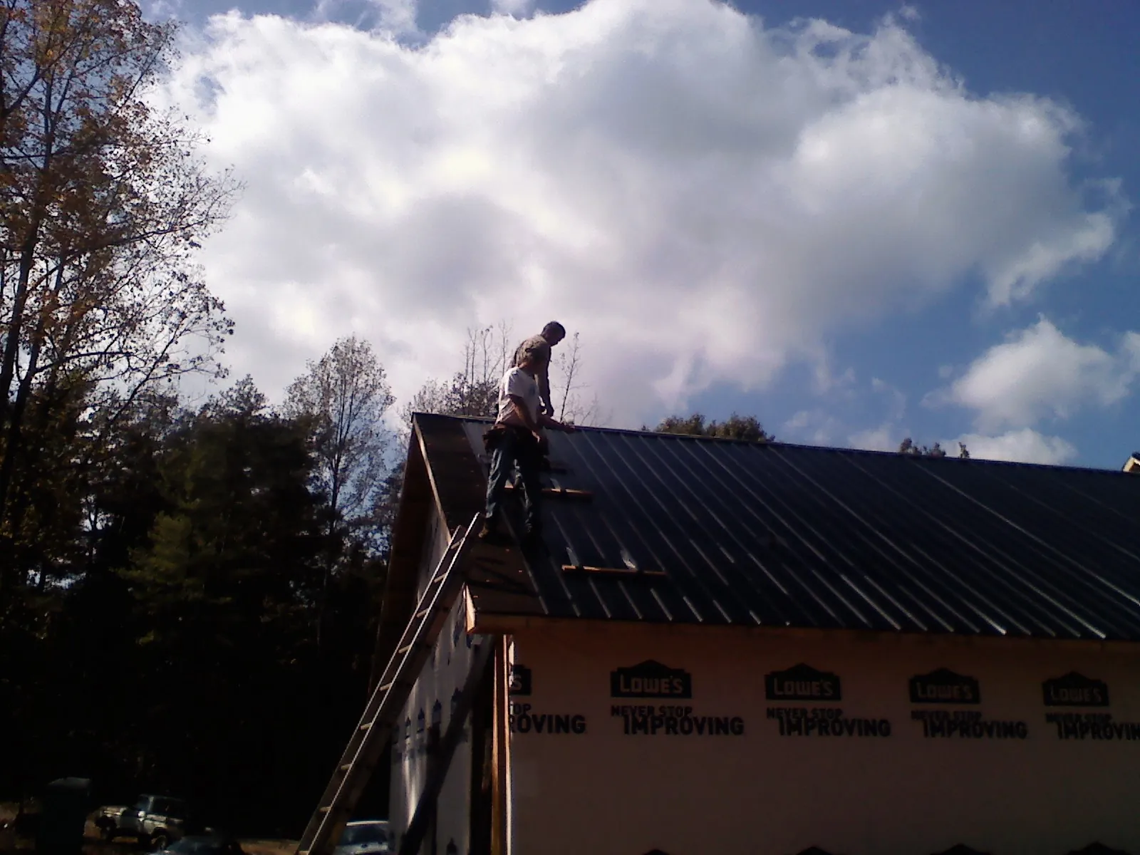 Roofer fastening dark metal panels high against a cloudy sky, from a Roof Inspection job in Dobbs Ferry