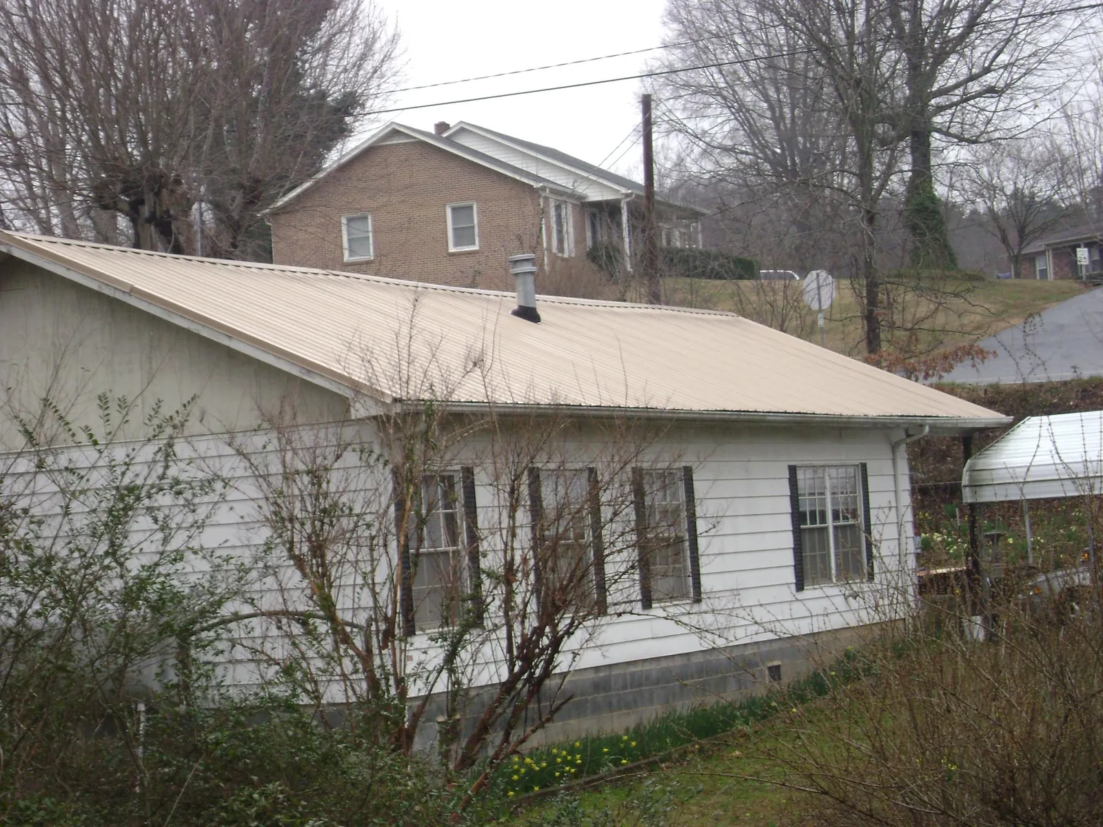 Tan metal roof on a white sided house set into a hillside — Commercial Roofing by Roofing Brothers in Dobbs Ferry
